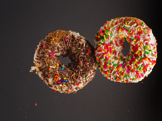 Two sweet colorful donuts in a frozen flight on a gray background. There are no people in the photo. There is free space to insert. Invitation for a holiday, birthday.