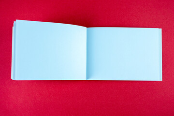 Open white horizontal notebook mock up on red paper background. Empty sketchbook for artists.