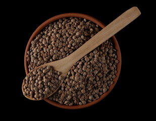 Brown uncooked lentils in clay pot and wooden spoon isolated on black