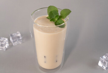 Glass of traditional Indian lassi drink with mango, mint and ice on a grey background.