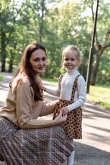 A little blonde girl and her mother are walking in the park in autumn. Family walk. Happy mom and daughter.