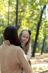 Fototapeta premium Mom and daughter are hugging in the park. Family walk. Happy mom and daughter. Green Park. Family values. Tenderness and love.