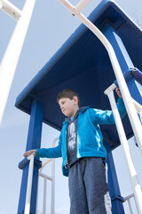 Young boy with Autism playing on a playground; boy is wearing blue outfit and surrounding...