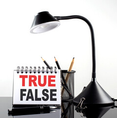 TRUE FALSE text on notebook with pen and table lamp on the black background