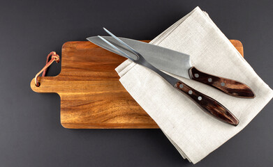 Wooden cutting board and fork and knife carving set on black background