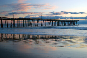 The colorful clouds of sunrise reflect in the waters near the Virginia Beach Fishing Pier