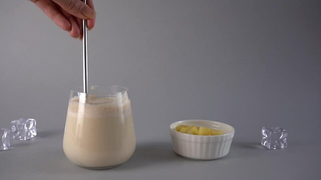 Traditional Indian mango lassi drink. Mixing drink with a spoon. Slow motion.