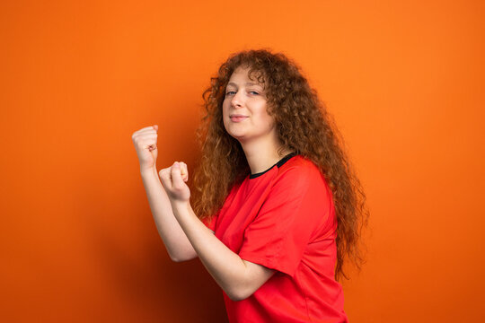 Picture of pretty redhead female fan in sport football uniform keeping fists for her football team victory, human emotions concept.