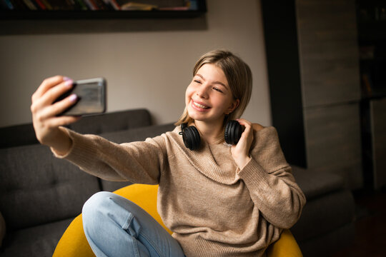A smiling young girl listens to music in her living room and is taking a picture of herself