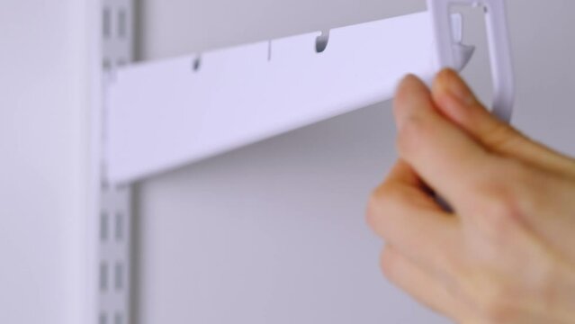 Installation brackets of a metal mesh shelf in the dressing room system on a bracket. Hands is assembling a white holder storage system close-up
