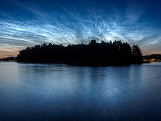 Noctilucent clouds over a tree covered island in a lake