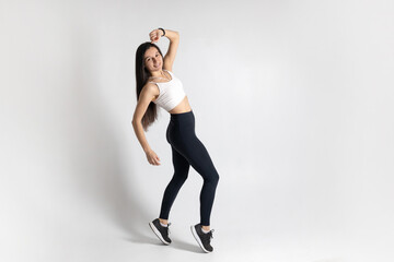 Full length view of smiling young woman posing and jumping on white background. Attractive brunette woman in fashionable sportswear exercising. Healthy lifestyle, sport concept