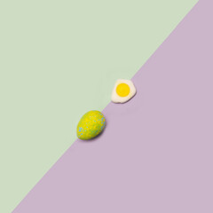 Easter minimal concept. Flat lay arrangements made of one unique blue painted egg with another fried egg in a diagonal line with green and purple very peri background..