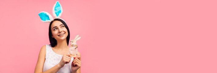 Cute woman in rabbit ears holding a rabbit toy, a traditional holiday, in the studio on a pink background