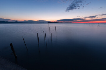 Fishing net poles on a lake, with perfectly still water and almost empty sky at dusk