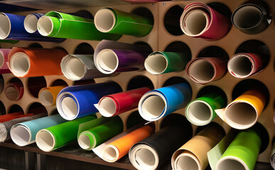 Multi-colored self-adhesive film in tubes on a shelf in a store. Consumable material for the...
