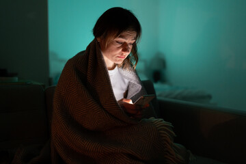 Sleepy exhausted woman sitting on sofa using smartphone, can not sleep. Insomnia, addiction. Sad...
