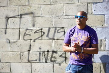 Spiritual swag. Shot of a young man standing in front of a wall with graffiti on it.
