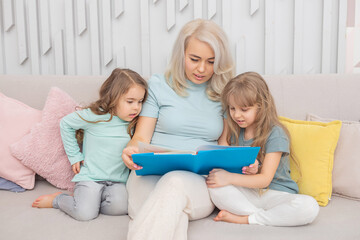 Smiling caucasian mom teaching daughters sitting on the sofa in the living room