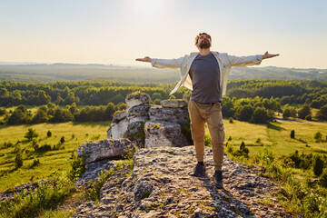 Young man standing on top of mountain on sunny day with arms wide open enjoying summer hike