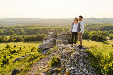 Young couple standing on top of the rock watching countryside landscape during summer hike in Jura,...
