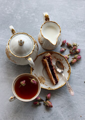 Cherry cake, cup of tea, milk jug and sugar bowl on a table. Close up photo of retro objects. Food still life on grey background. 