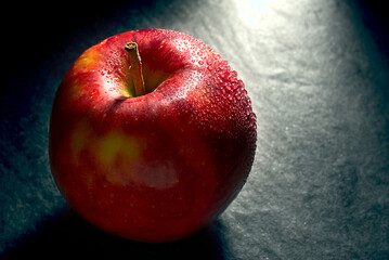 Red juicy apple with water droplets on a dark background.