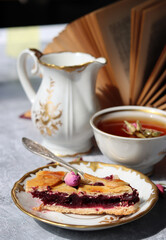 Still life with cup of tea,  jug of milk, cherry pie, small rose flowers. White vintage tableware on a table.  Sweet breakfast close up photo. 