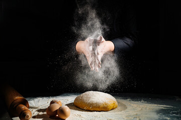women kneads dough and scatters flour on a black background.