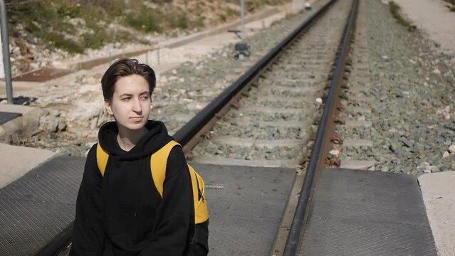 sad teenage girl with yellow backpack sitting on the railway track. Refugee concept. Medium shot