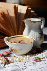 Simple composition still life with milk jug, cup of tea and an open book on a table. Close up photo of retro styled objects. Sunny day photo. 