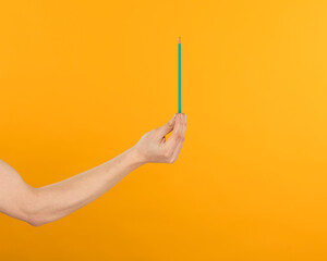 
a man's hand holds a green pencil on a bright yellow background close-up
