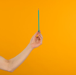 
a man's hand holds a green pencil on a bright yellow background close-up
