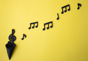 Black musical notes coming out of black ice cream cone.Yellow background with creative negative space.
