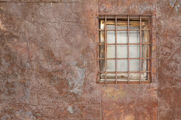 Authentic natural brown background with red tints. A metal prison bars on the window of an old house that looks like a prison sheathed with metal sheets.