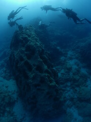 scuba divers around a reef underwater deep blue water big rocks  air bubbles rising
