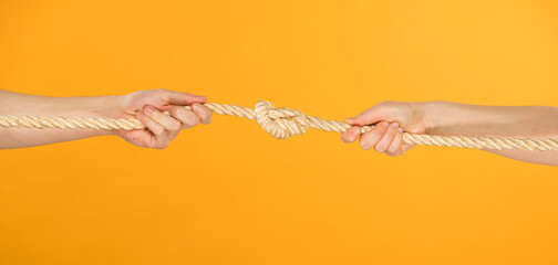 male and female hands pull the rope with a knot in the middle on a yellow background close-up