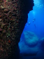 Fototapeta na wymiar scuba divers around a reef underwater deep blue water big rocks air bubbles rising