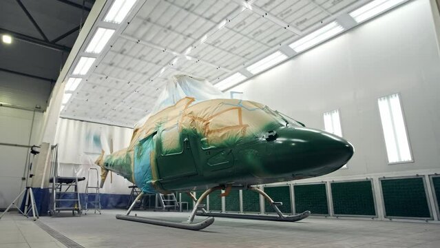military or civilian helicopter stands in spray booth and is painted khaki green. aircraft is being repaired at docks. business helicopter painted and recolored. Military equipment for maintenance.