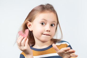 Cute little girl with blond hair is holding a pink dental myofunctional trainer