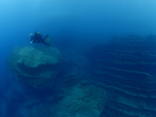 Naklejka na ściany i meble scuba divers around a reef underwater deep blue water big rocks air bubbles rising