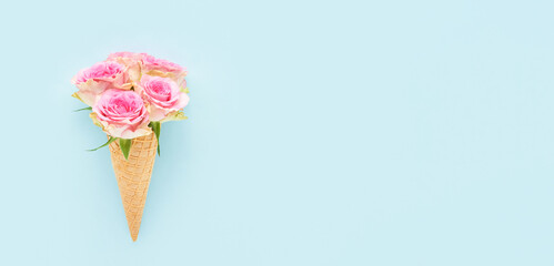 Pink roses in a waffle ice cream cone on a blue background. Summer concept, banner