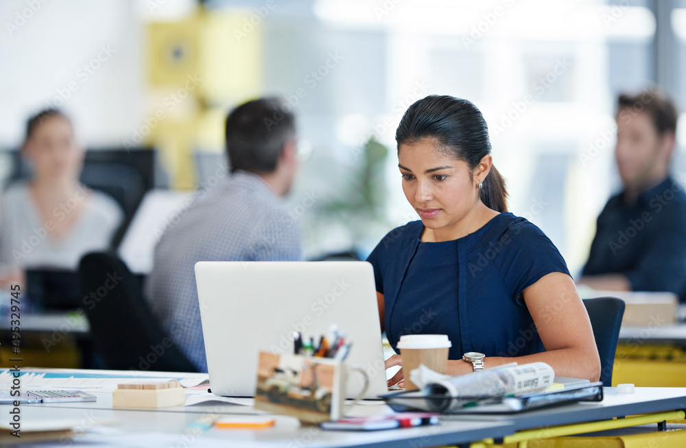 Canvas Prints Immersed in her work. Shot of a designer sitting at her desk working on a laptop with colleagues in the background.