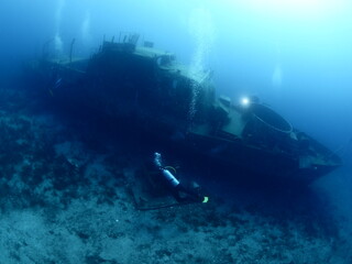 scuba divers exploring and discovering the ship wreck underwater deep sea bottom metal on ocean floor