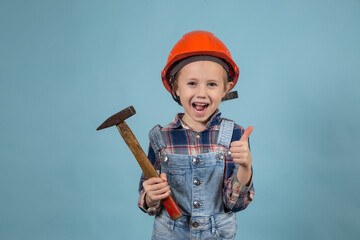 Adorable caucasian child is wearing orange safety helmet,holding hammer at hands
