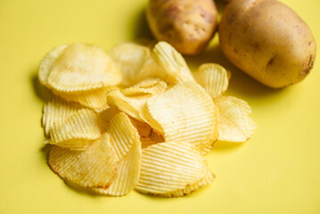 Potato chips snack on yellow background, Crispy potato chips on the kitchen table and fresh raw potatoes