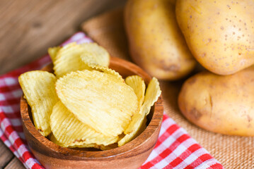 Potato chips snack on bowl, Crispy potato chips on the kitchen table and fresh raw potatoes on wooden background