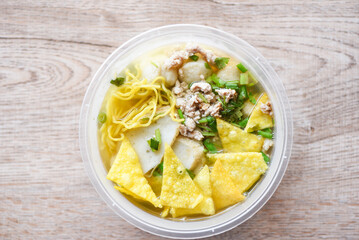 noodles pork balls fish balls and minced pork with crispy wontons and vegetable in plastic bowl on wooden table, top view Thai and China Asian food delivery concept