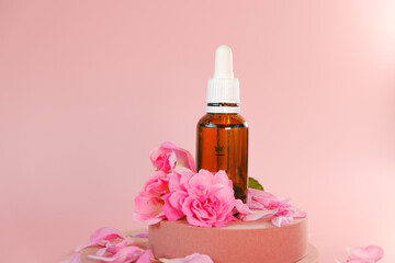 Rose essential oil in a glass bottle and rose flowers on a pink podium on a pink background....