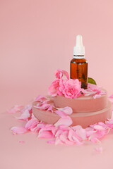 Rose oil in a glass bottle and rose flowers on a pink podium on a pink background.natural rose oil....